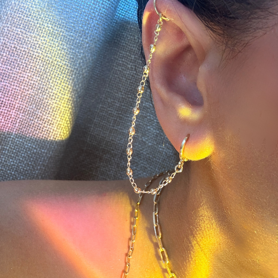 Close-up of an ear wearing a gold chain earring with a colorful background.